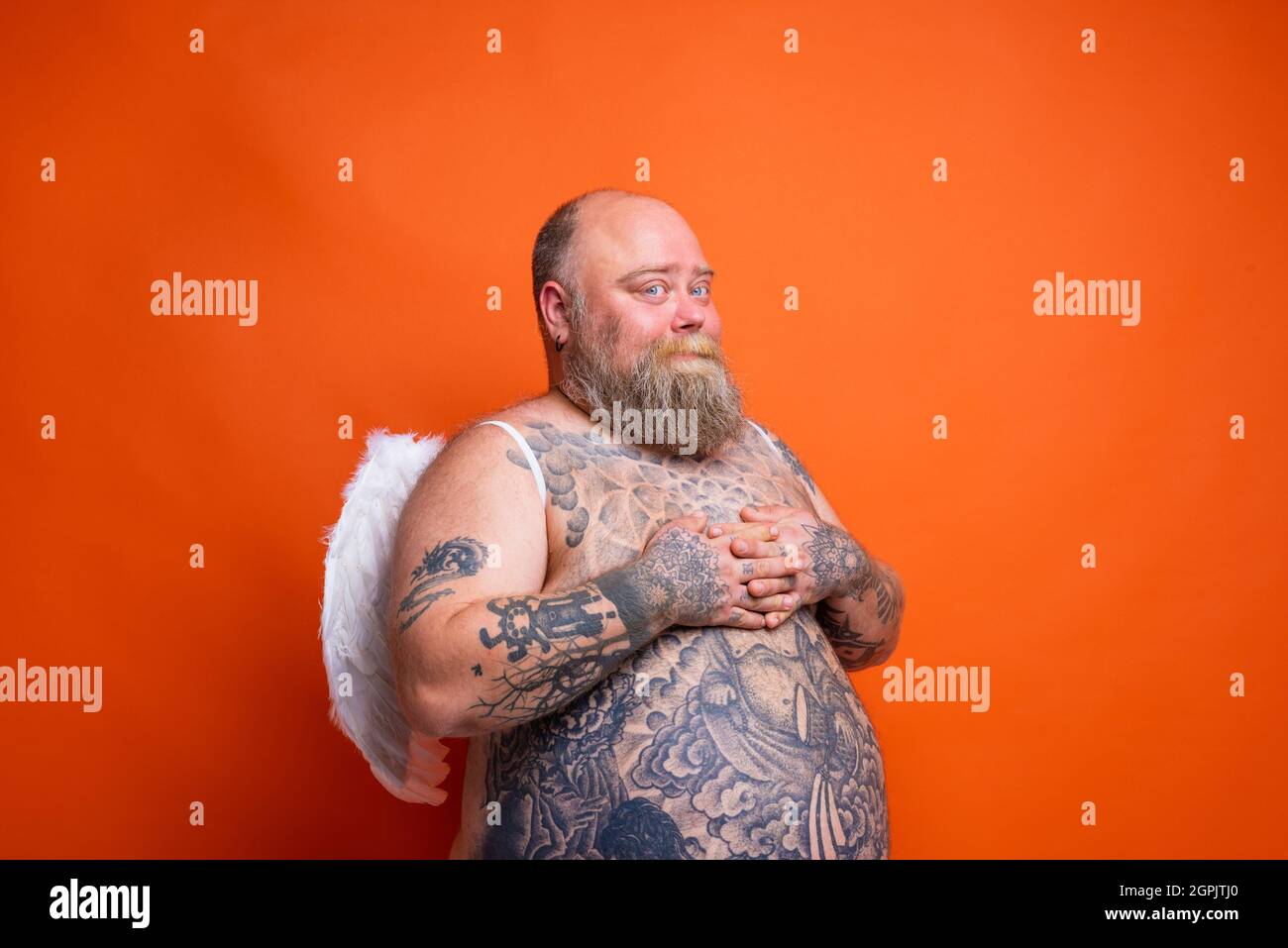 Fat man with beard ,tattoos and wings acts like an angel Stock Photo