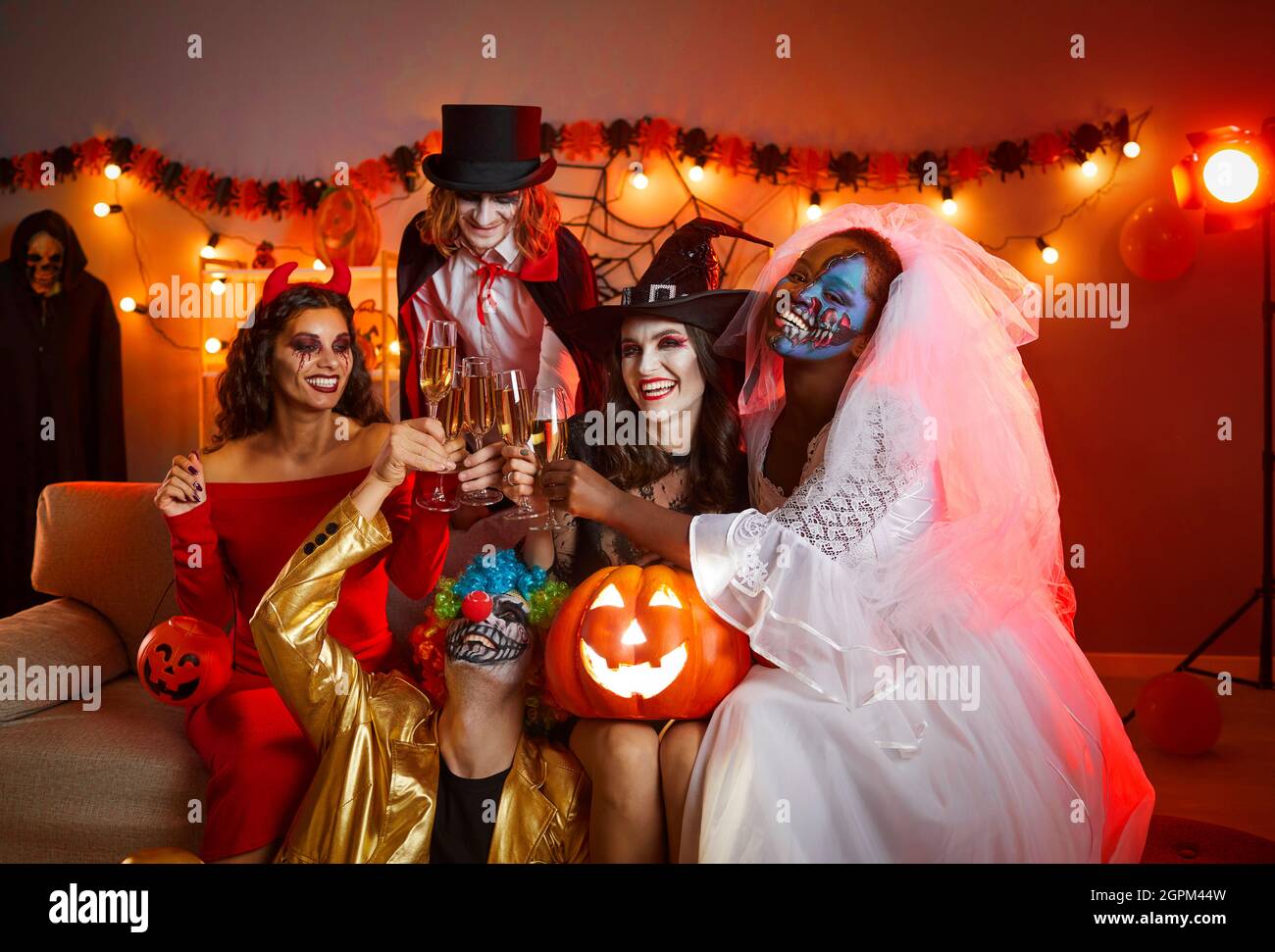 Group of cheerful friends in spooky halloween costumes posing with glasses of champagne in hands. Stock Photo