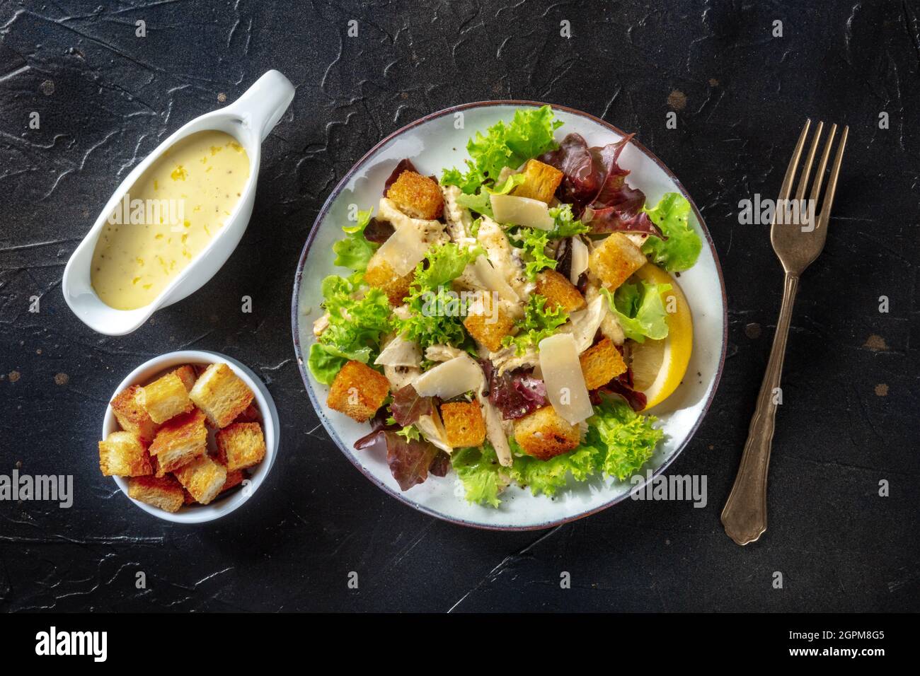 Chicken Caesar salad, overhead flat lay shot with the classic mayonnaise based sauce and croutons, on a black background Stock Photo