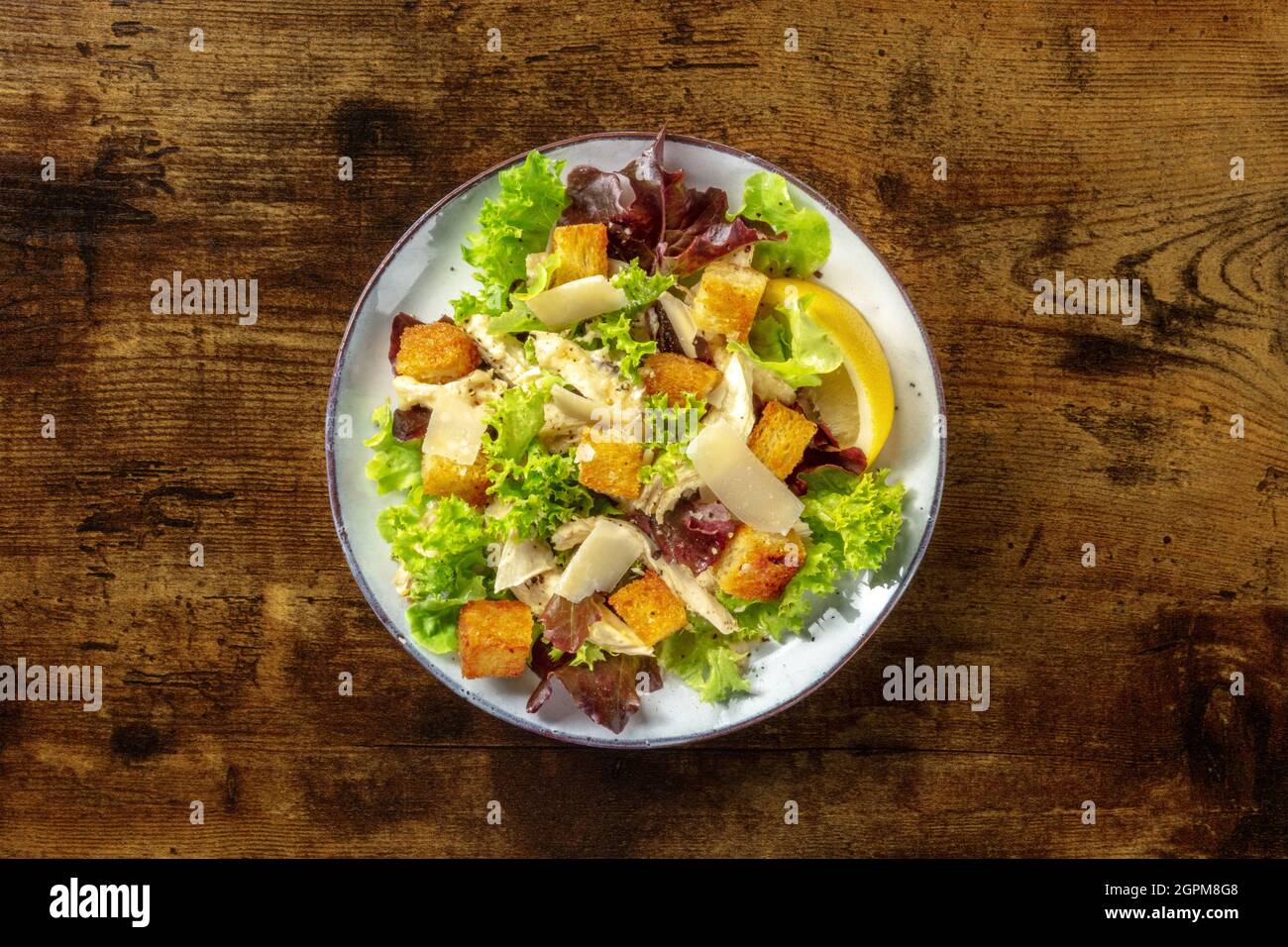 Chicken Caesar salad, overhead shot on a dark rustic wooden background. Romaine leaves, crispy croutons and chicken fillet meat Stock Photo