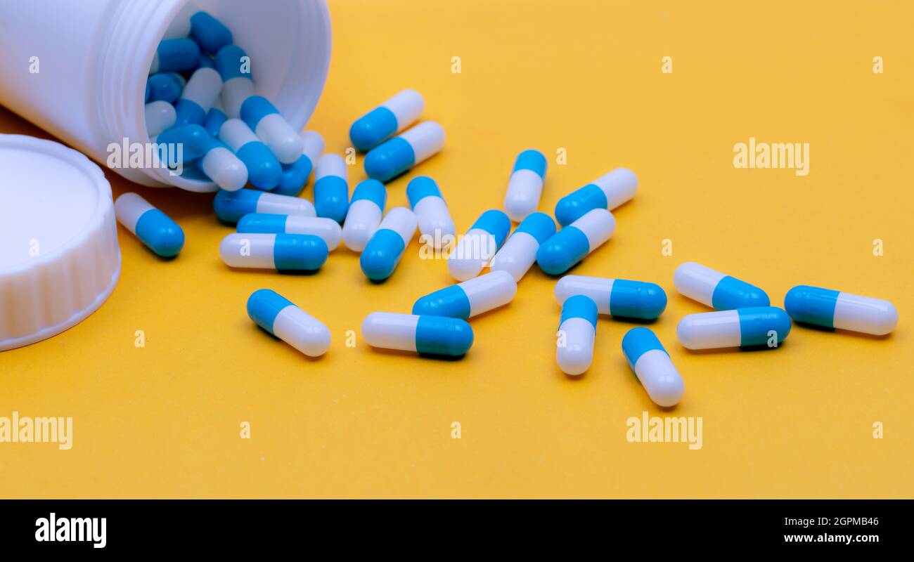 Pour capsule pills out of plastic bottle. Capsule pills on yellow background. Prescription drugs. Pharmaceutical industry. Pharmaceutic concept. Stock Photo