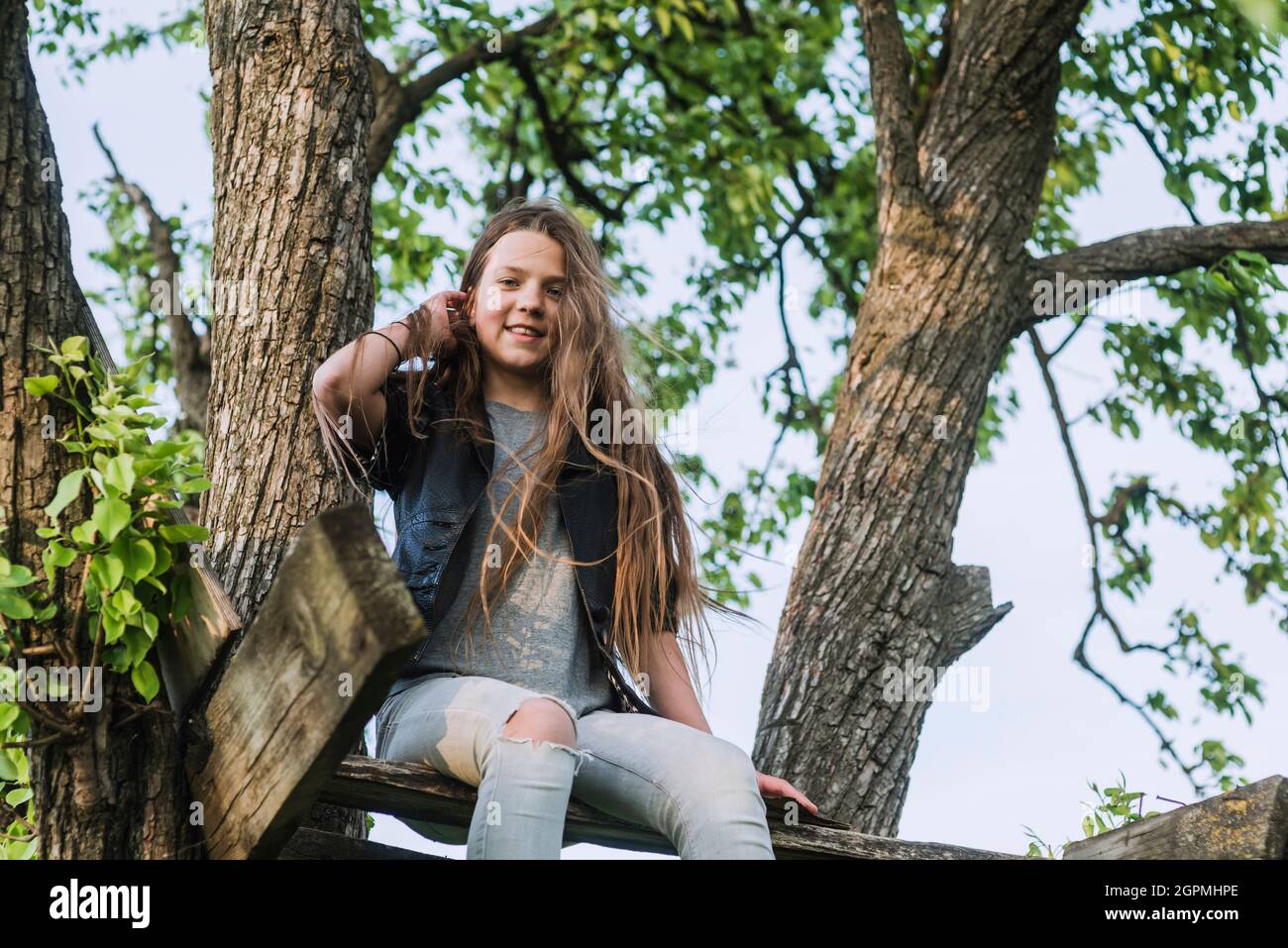 happy teenage girl sitting on wooden terrace arranged on tree branches Stock Photo