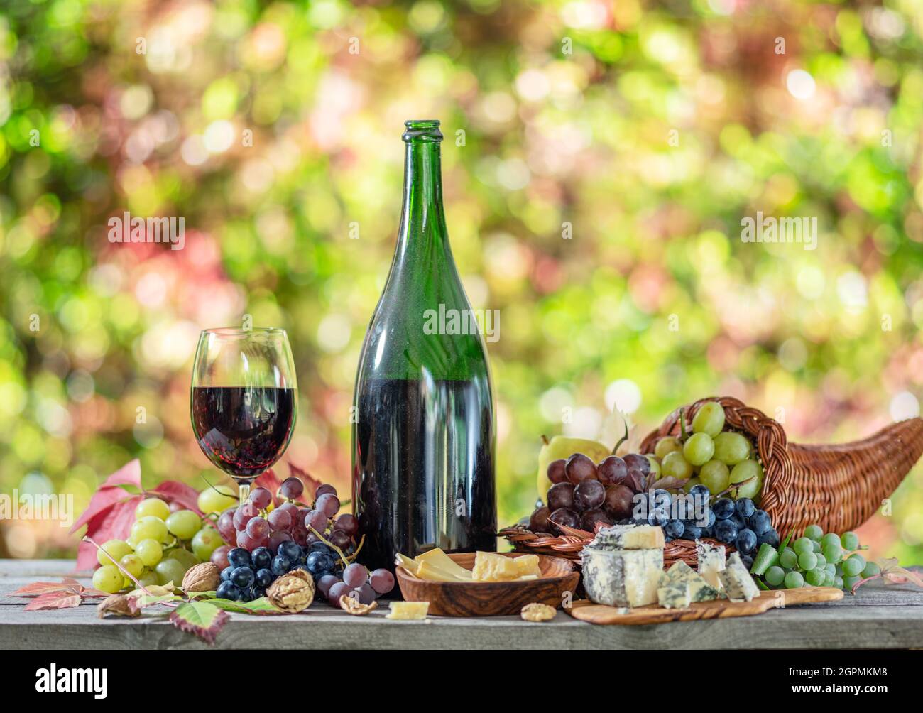 Grapes, bottle of wine and different cheeses on country wooden table and blurred colorful autumn background. Variety of products as the symbol of autu Stock Photo