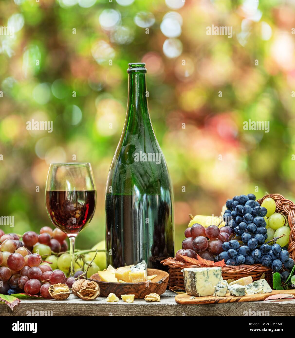 Grapes, bottle of wine and different cheeses on country wooden table and blurred colorful autumn background. Variety of products as the symbol of autu Stock Photo