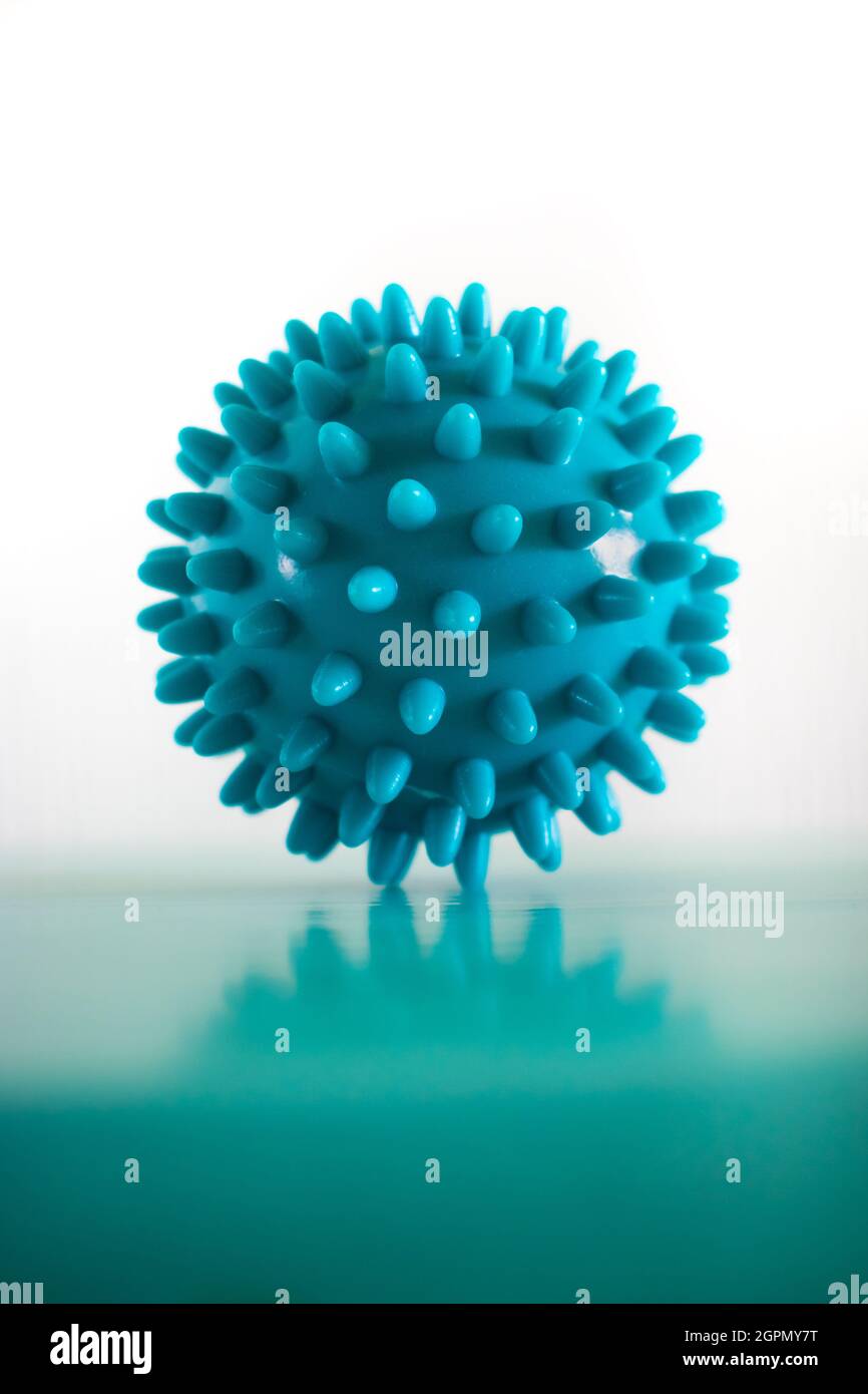 Turquoise, spiky hard massage ball on a turquoise desk on a white background, and the massage ball is reflecting from the table surface Stock Photo