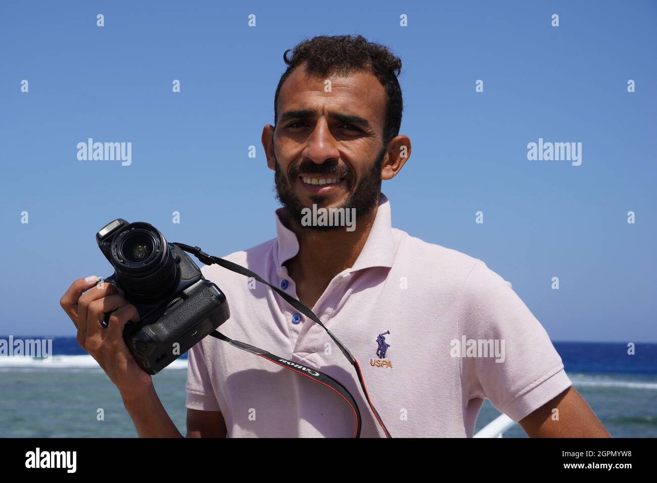MARSA ALAM, EGYPT - September 25, 2021. Portrait of smiling Arabic man Holding photo Camera on Red sea background. Photographing tourists during sea t Stock Photo