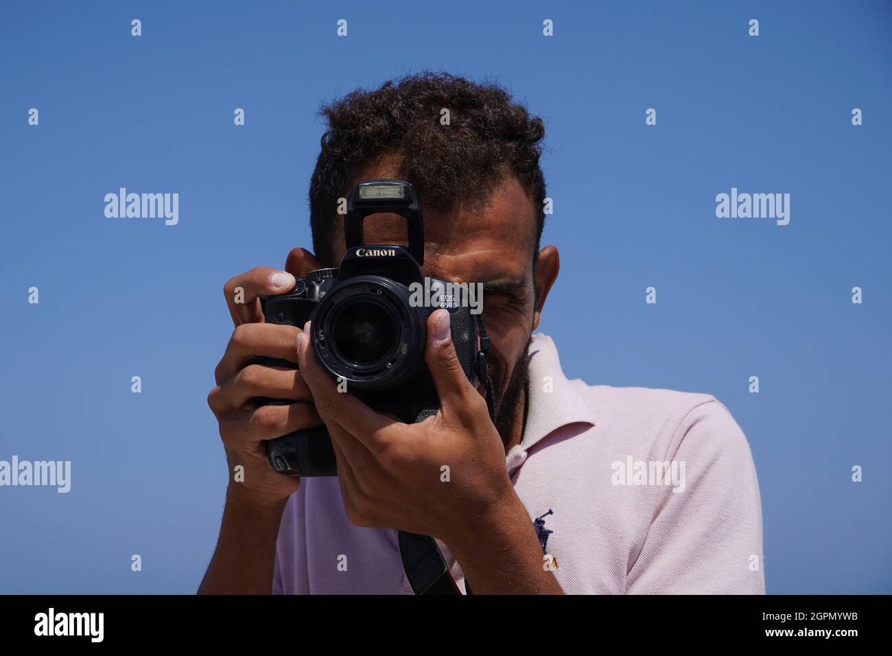 MARSA ALAM, EGYPT - September 25, 2021. Portrait of smiling Arabic man Holding photo Camera on clear blue sky background. Photographing tourists durin Stock Photo