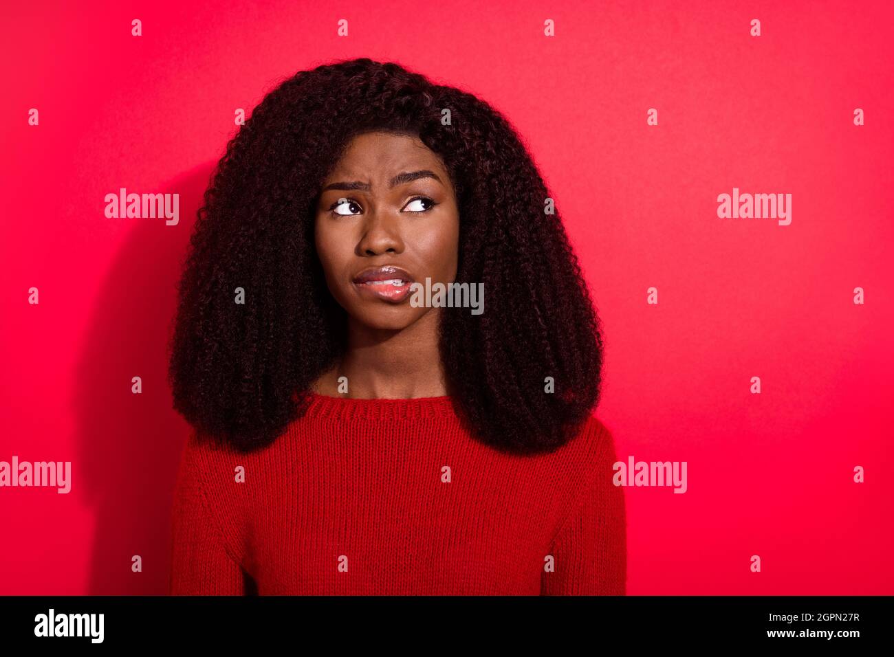 Photo of charming doubtful dark skin lady wear casual sweater biting lip looking empty space isolated red color background Stock Photo