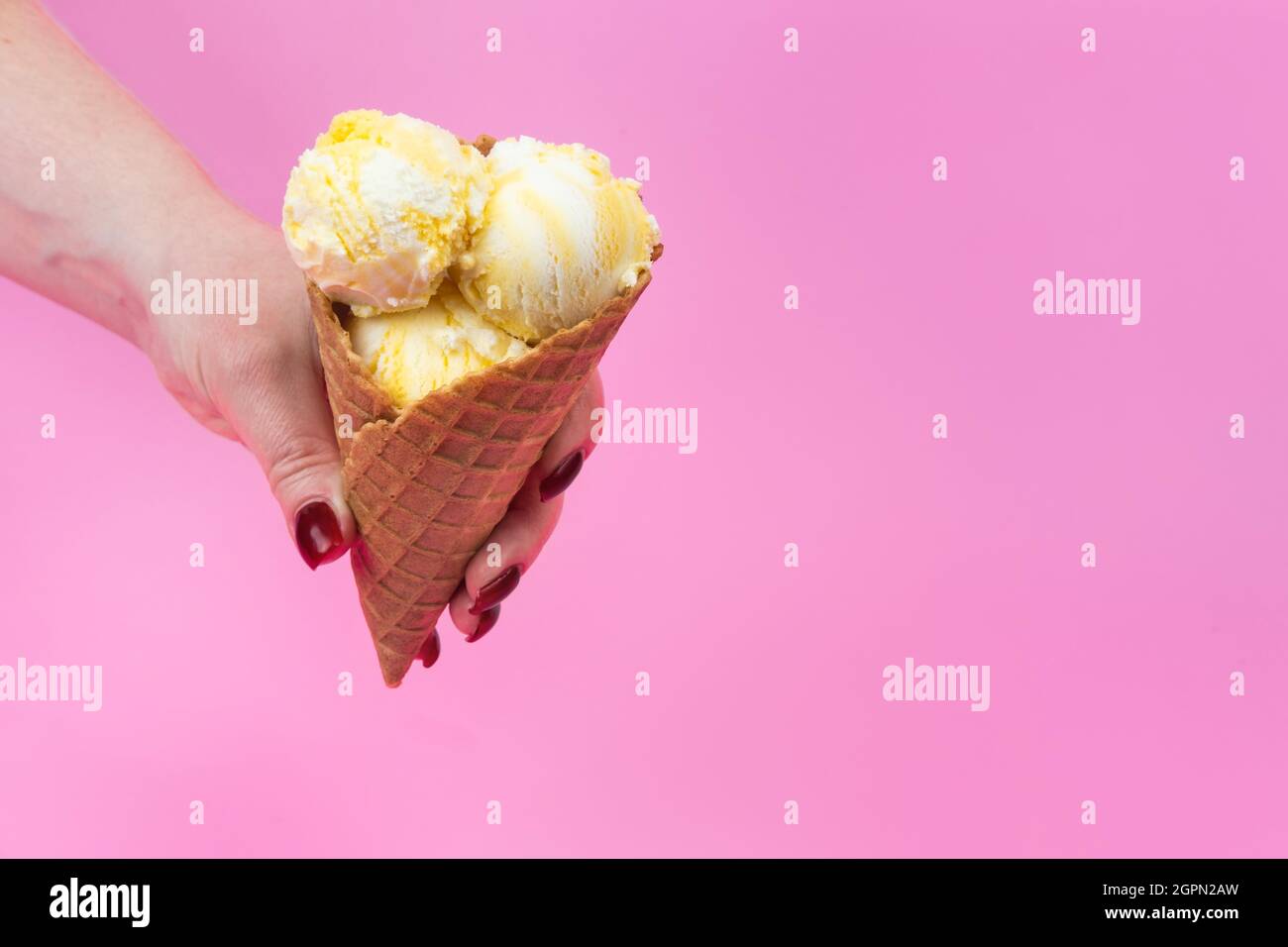 A hand holds an ice cream cone on a pink popsicle background in a ...