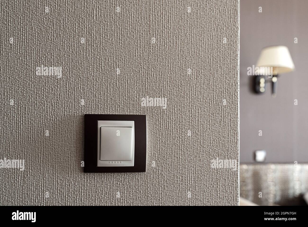 front view closeup of white light plastic switch socket on textured wall with home interior in the background Stock Photo