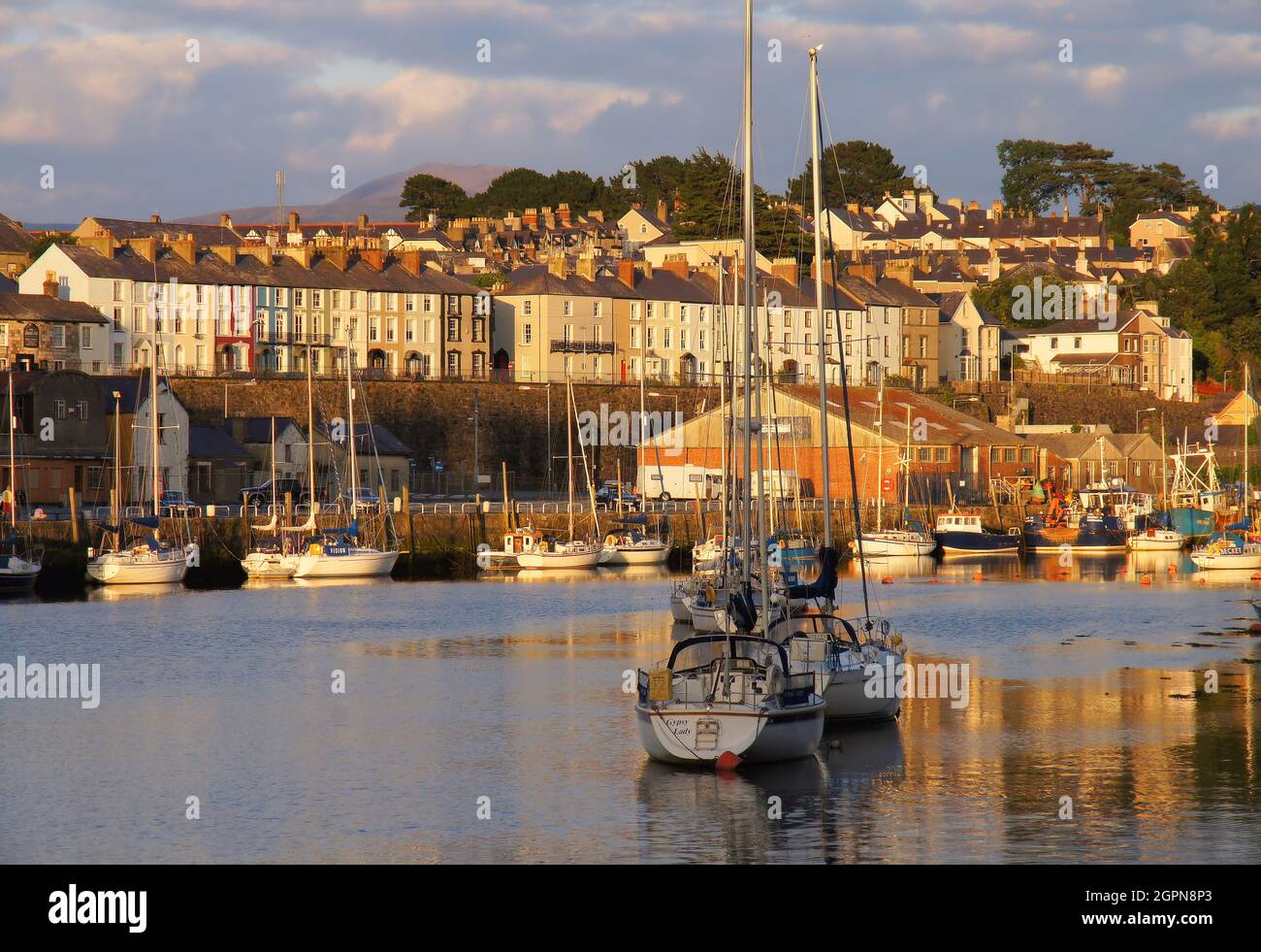 Boats in the harbour, reflections and colourful terrace houses along the River Seiont soon before sunset in Caernarfon, Gwynedd, Wales Stock Photo