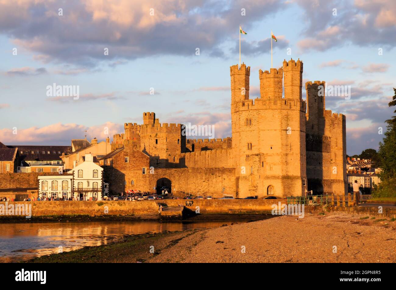 Caernarfon Castle, parts of the town and reflections in the sea (river) soon before sunset at Caernarfon Gwynedd, Wales Stock Photo