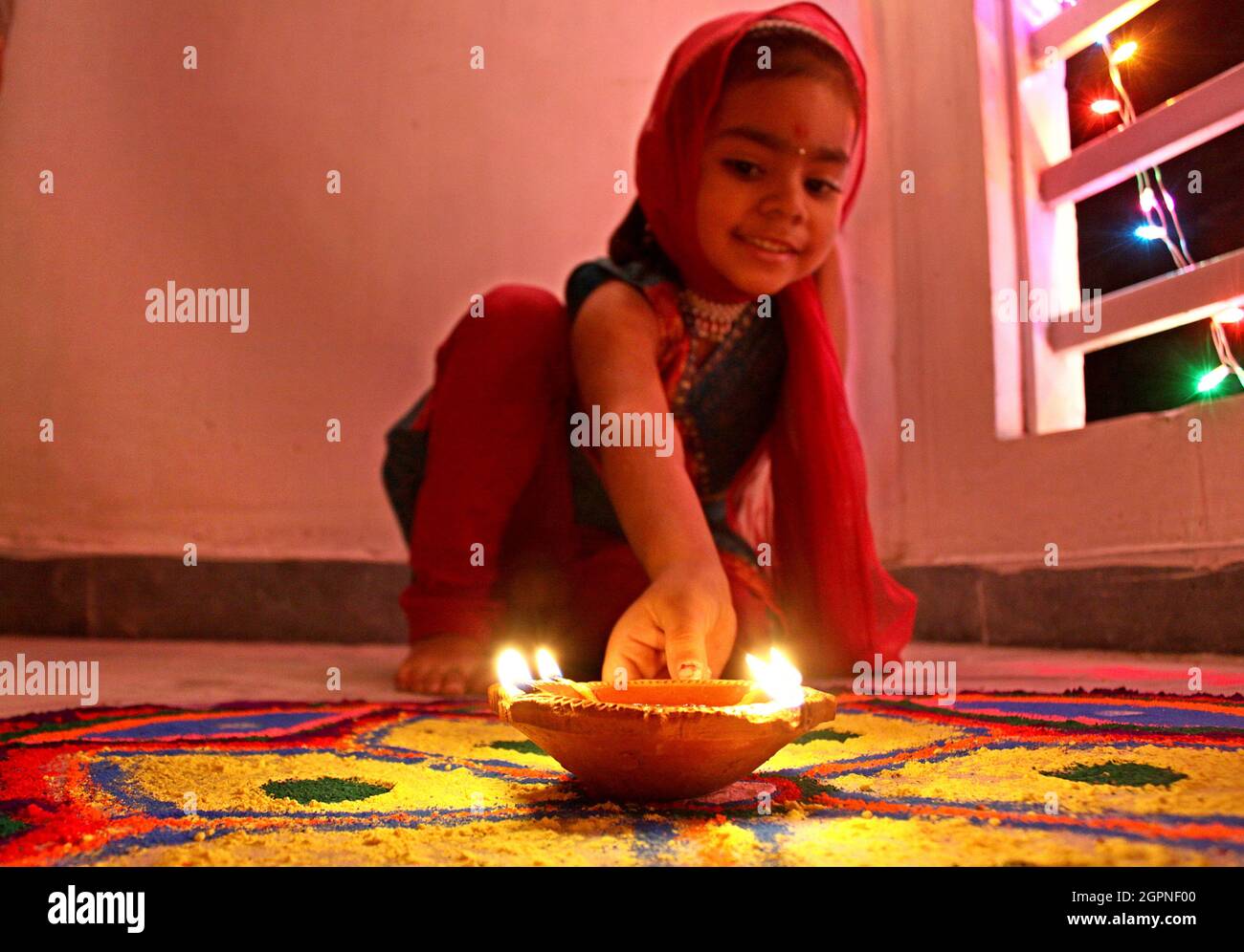 A girl child put a earthen lamp on the decorated floor of her house on the occasion of Diwali festival in New Delhi. Stock Photo
