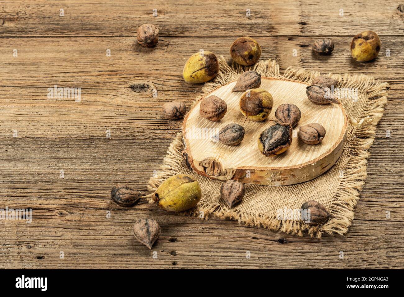 Ripe Juglans cordiformis Maxim or heart-shaped walnut. Young green and unpeeled whole nuts on a stand. Vintage wooden boards background, copy space Stock Photo
