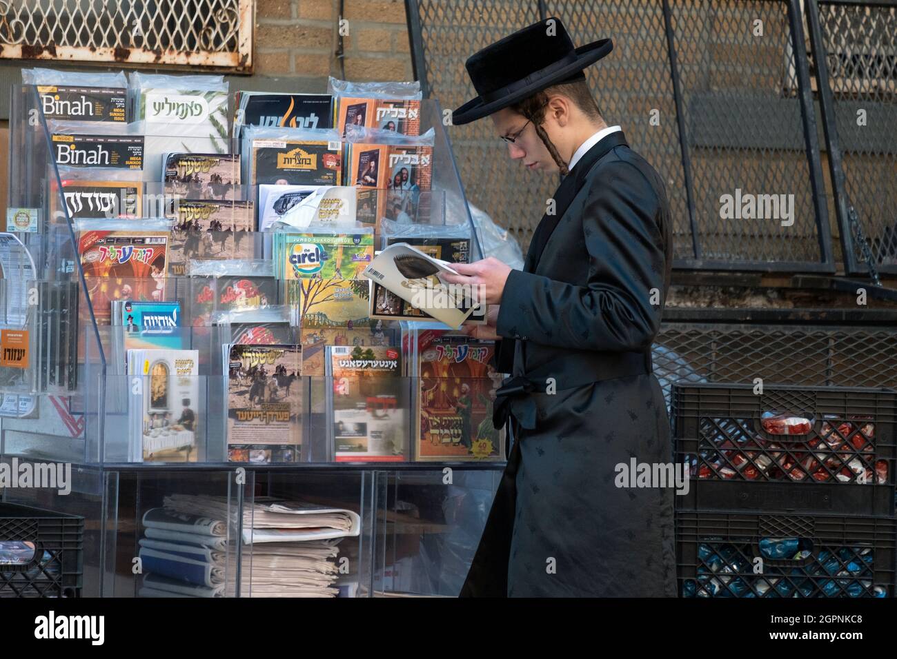 A Hasidic young man reads a periodical from a rack of magazines with