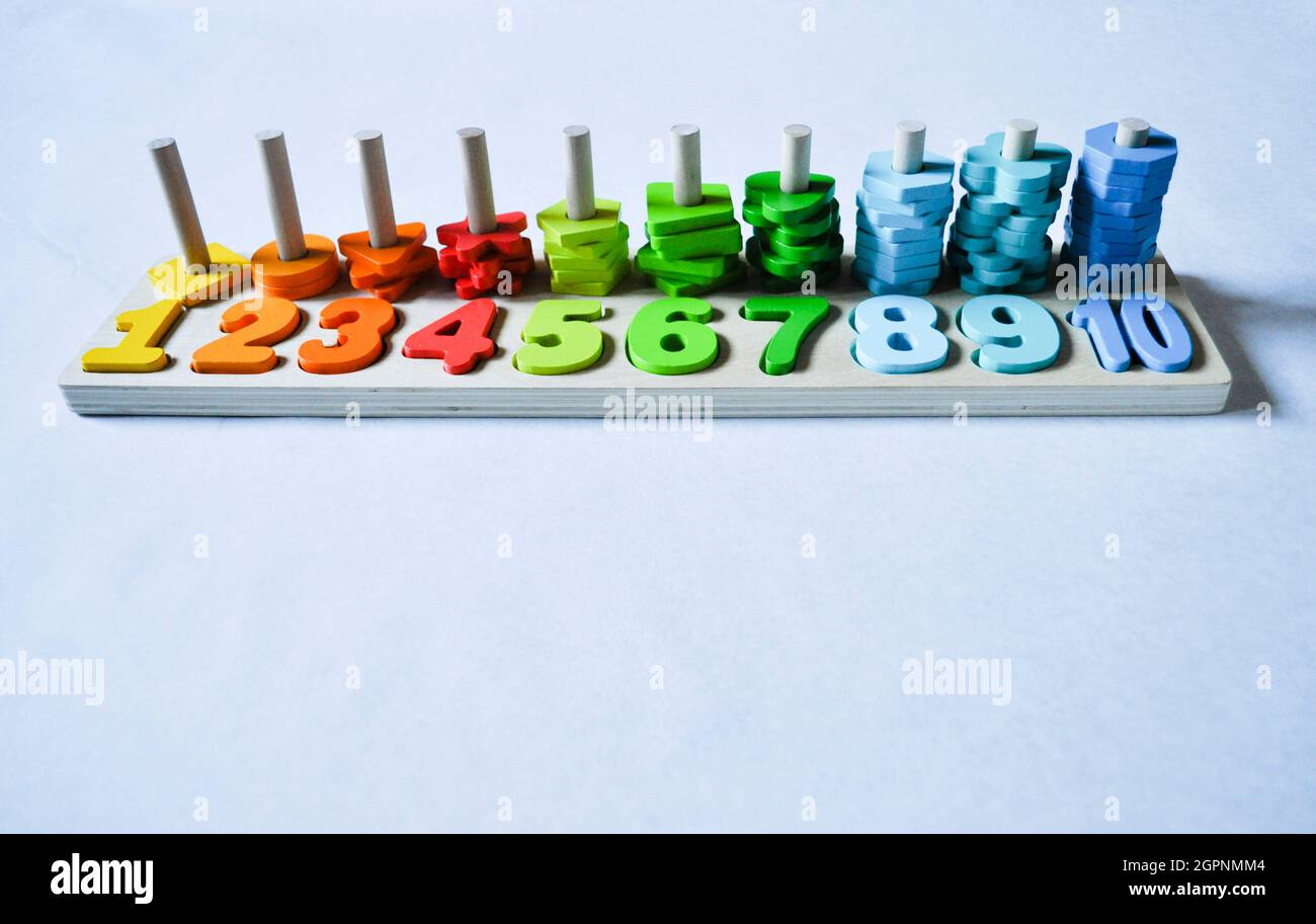 Wooden number line showing numbers 1-10 in order with stacking objects behind on a white background. Copy space is available. This is a toddler toy Stock Photo