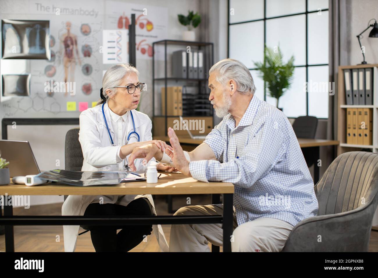 Qualified female doctor in uniform bandaging injured arm of aged male patient. Professional