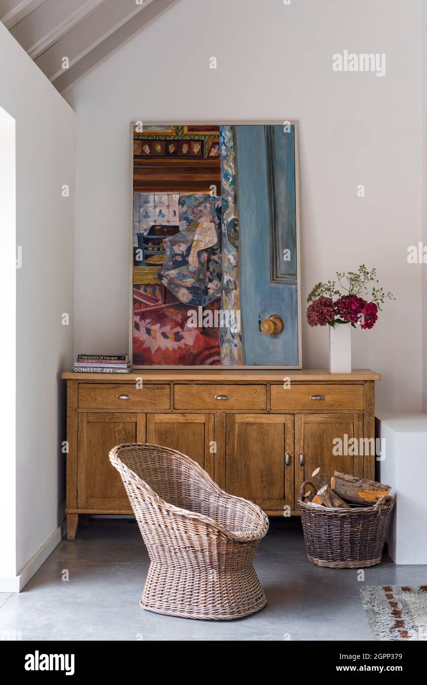 Mid century wicker chair with Lottie Cole artwork on sideboard in Sussex farmhouse, UK Stock Photo