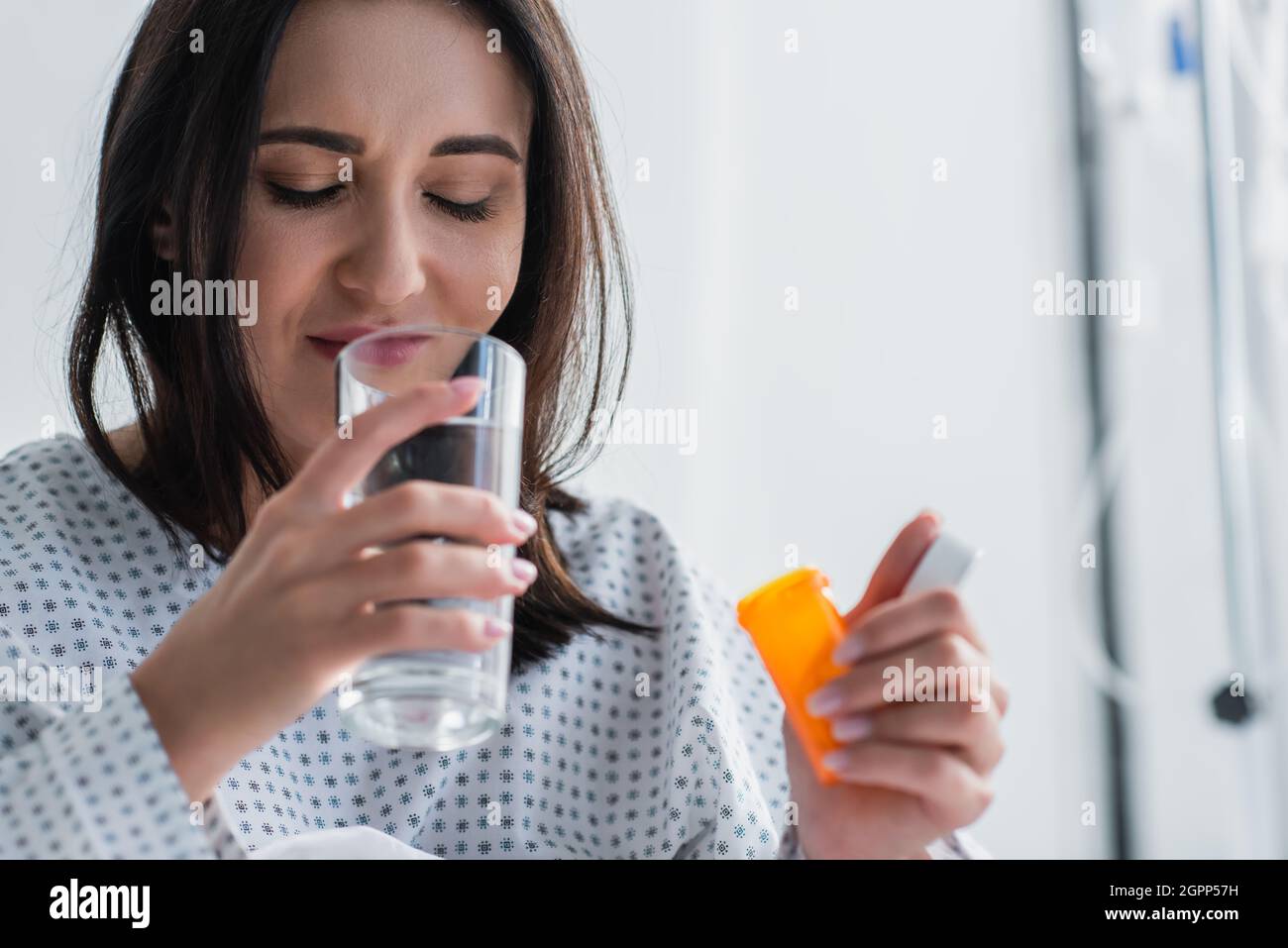 woman holding bottle with medication while taking pill in hospital