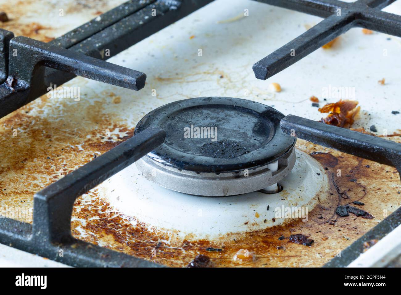 Dirty gas stove surface. Medium gas burner and cast iron grate of a gas oven surrounded by old leftovers of food and drinks. Top area surface and burn Stock Photo