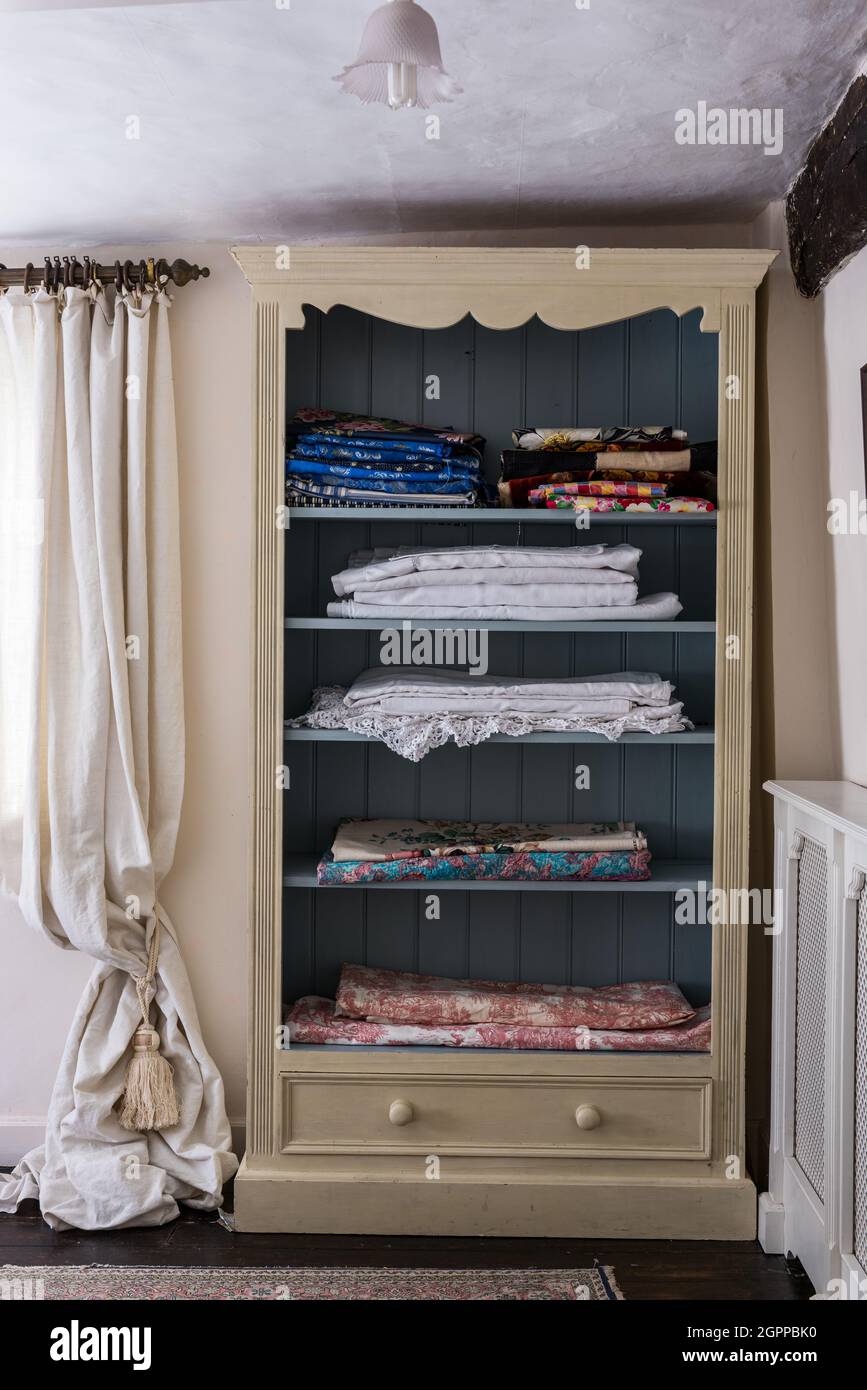 Fabrics and linens folded on shelves in Suffolk cottage. Stock Photo