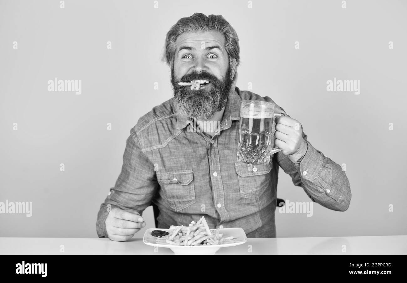 French fries potato. guy in american bar drinking beer glass and eating potato. Cheers. watching football on TV. american fast food. happy bearded man Stock Photo