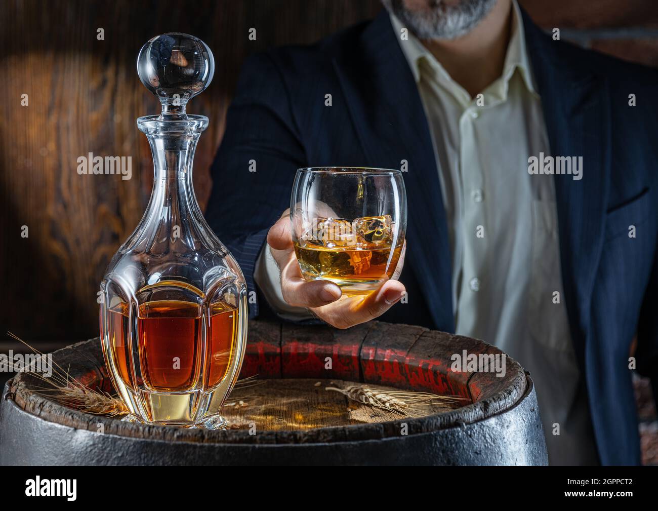Whisky tasting. Man sits in front of a barrel with a decanter and a glass of whiskey. Stock Photo