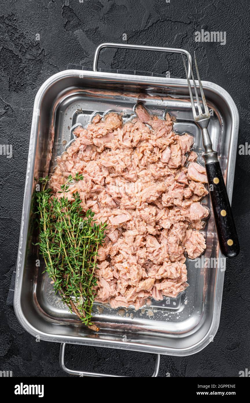 Tuna canned fish with olive oil in a tray . Black background. top view