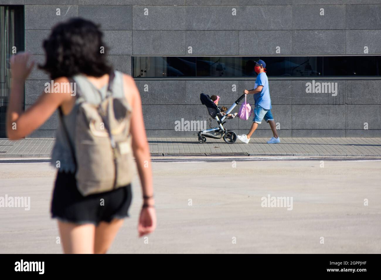 Father with mask pushing his baby in stroller in a street near a wall. Stock Photo