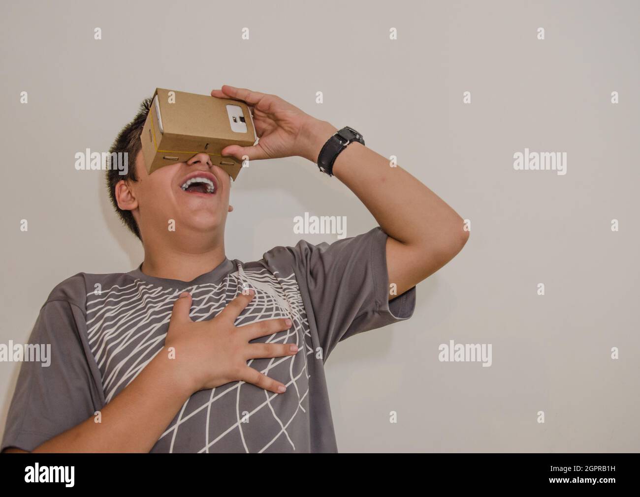 Laughing Teenager Boy Covering Eyes With Smart Phone In Cardboard Box Stock Photo