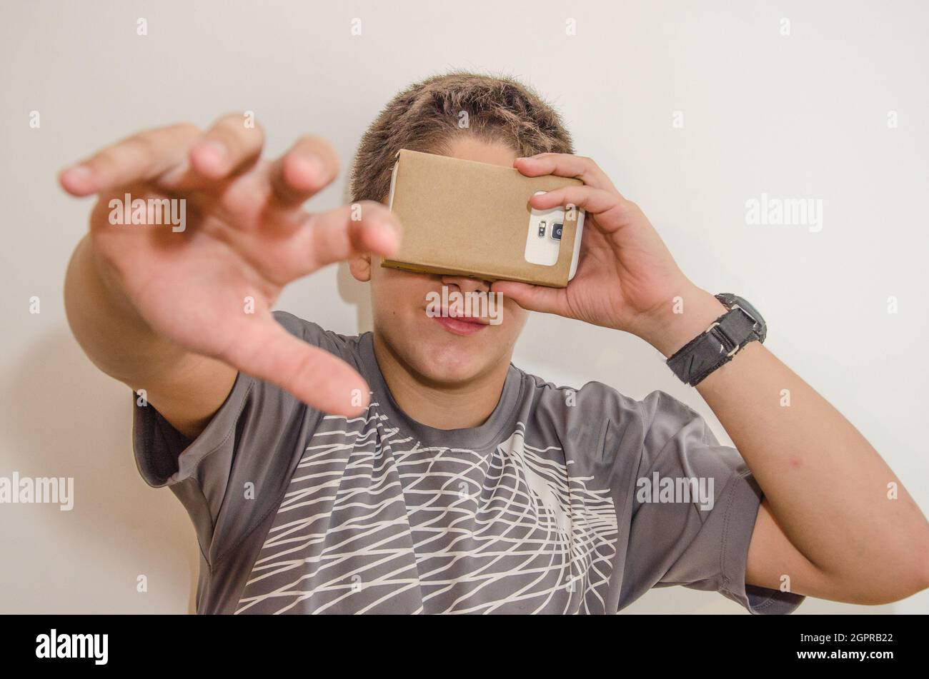 Smiling Teenager Boy Covering Eyes With Smart Phone In Cardboard Box Stock Photo
