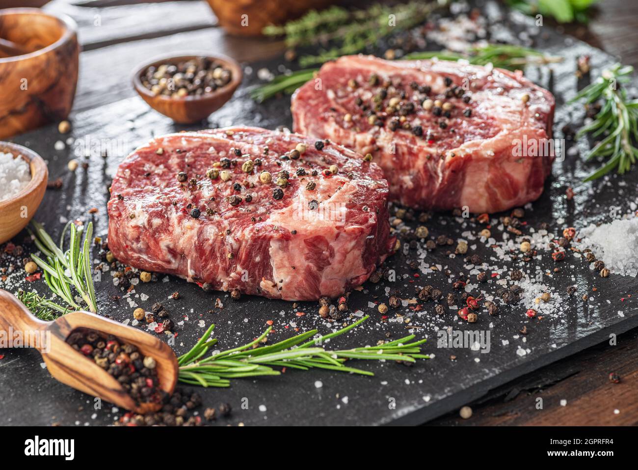 Raw Ribeye steaks with salt and herbs on grey board. Top view Stock