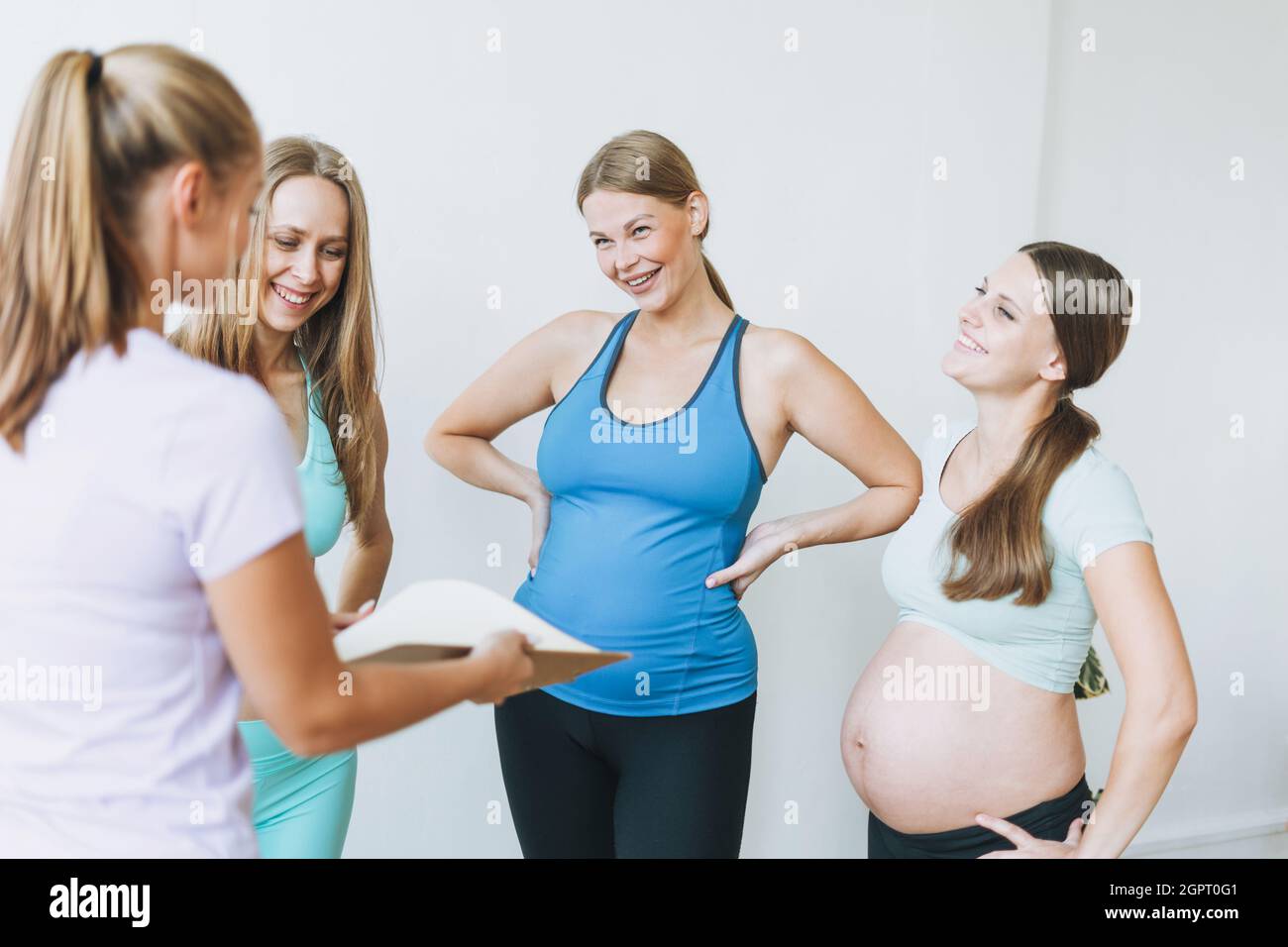 Group Of Pregnant Women In Sports Uniforms Communicate With Coach In Bright Studio Stock Photo