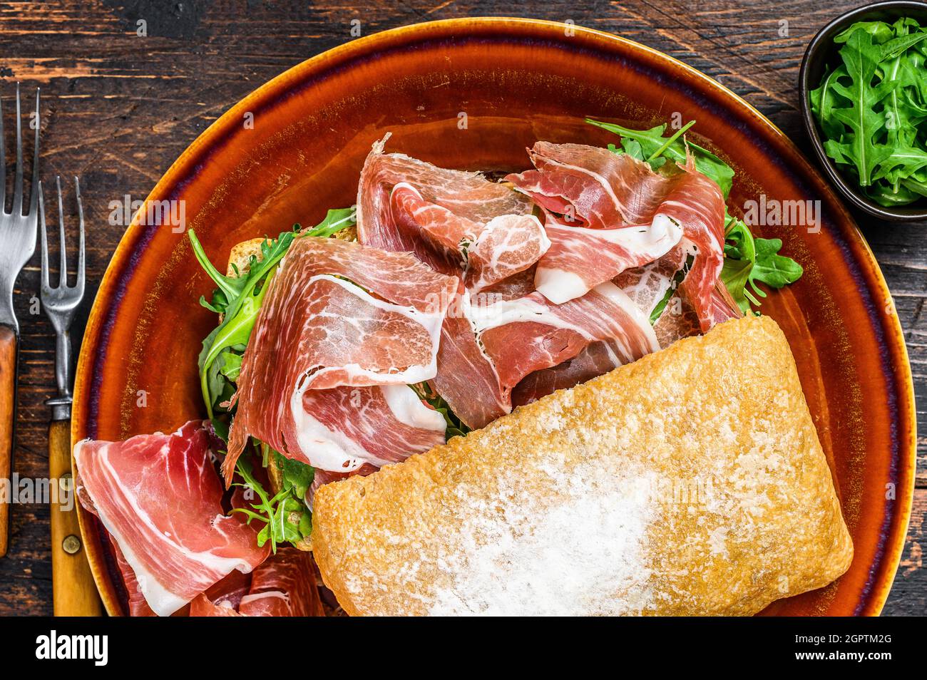 Spanish bocadillo de jamon, serrano ham sandwich on ciabatta bread with arugula. Dark wooden background. Top view Stock Photo