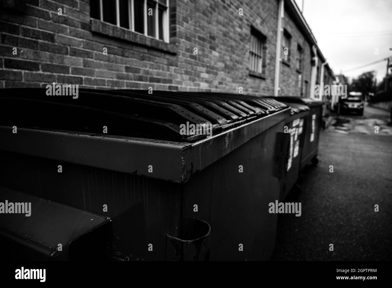 row of covered garbage bins along a brick wall in a back alley Stock Photo