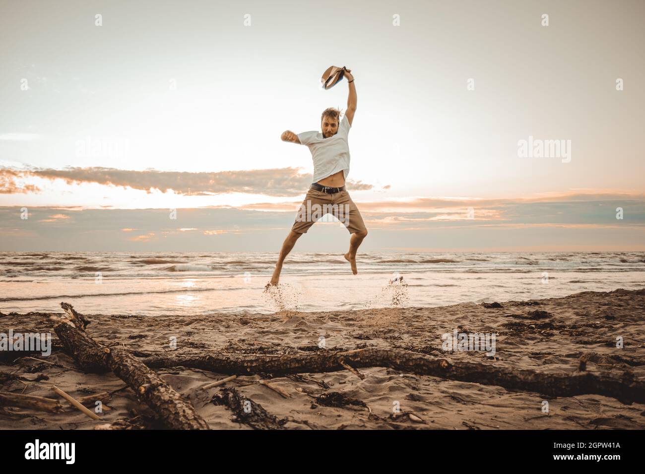 Happy boy enjoying summer holidays on beach at sunset - Young man jumping on the beach at the sunrise - Vacations concept Stock Photo