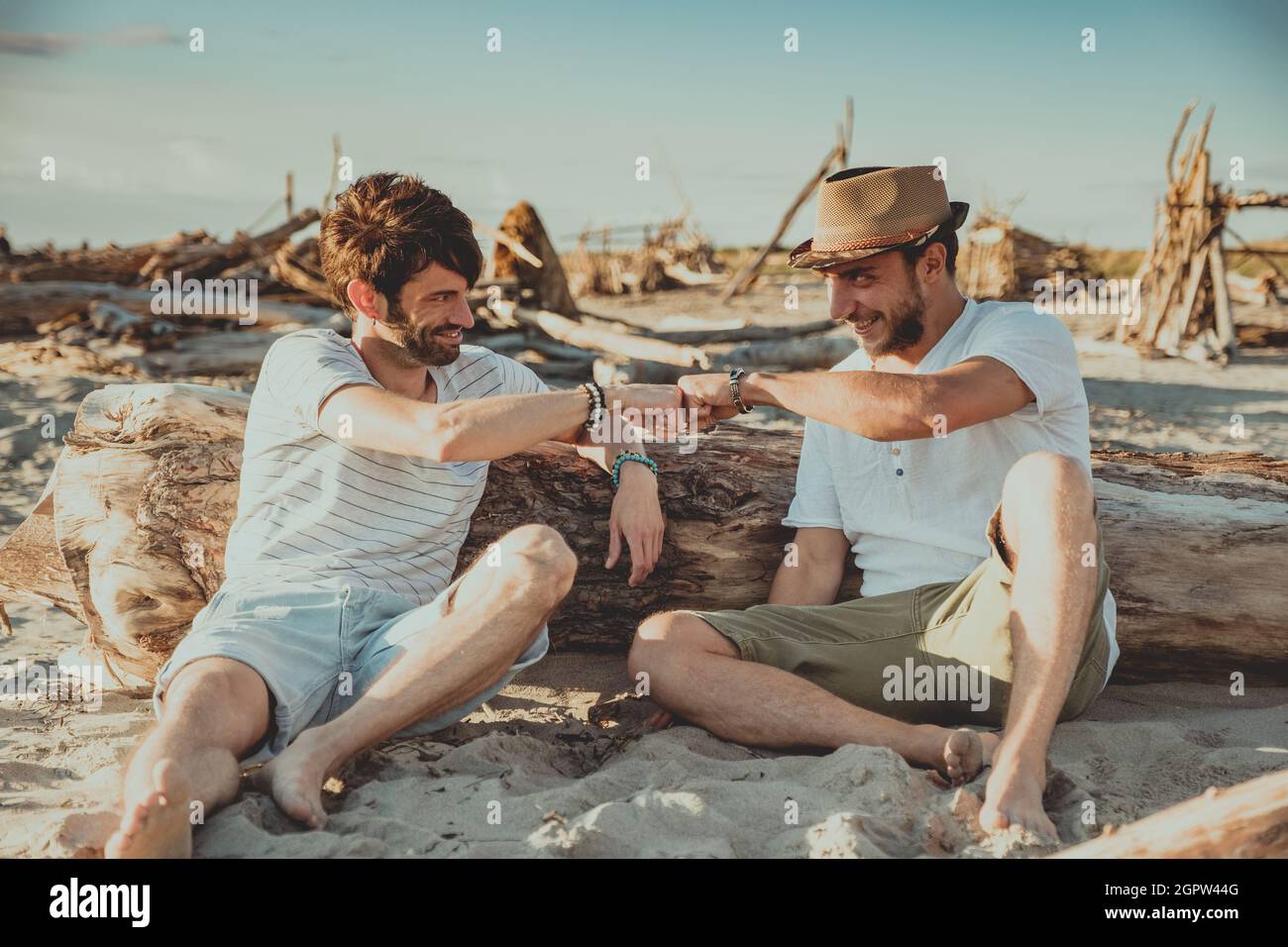 Two boys sitting on the beach greeting each other with their fists. Young people pounding their fists to greet each other Stock Photo