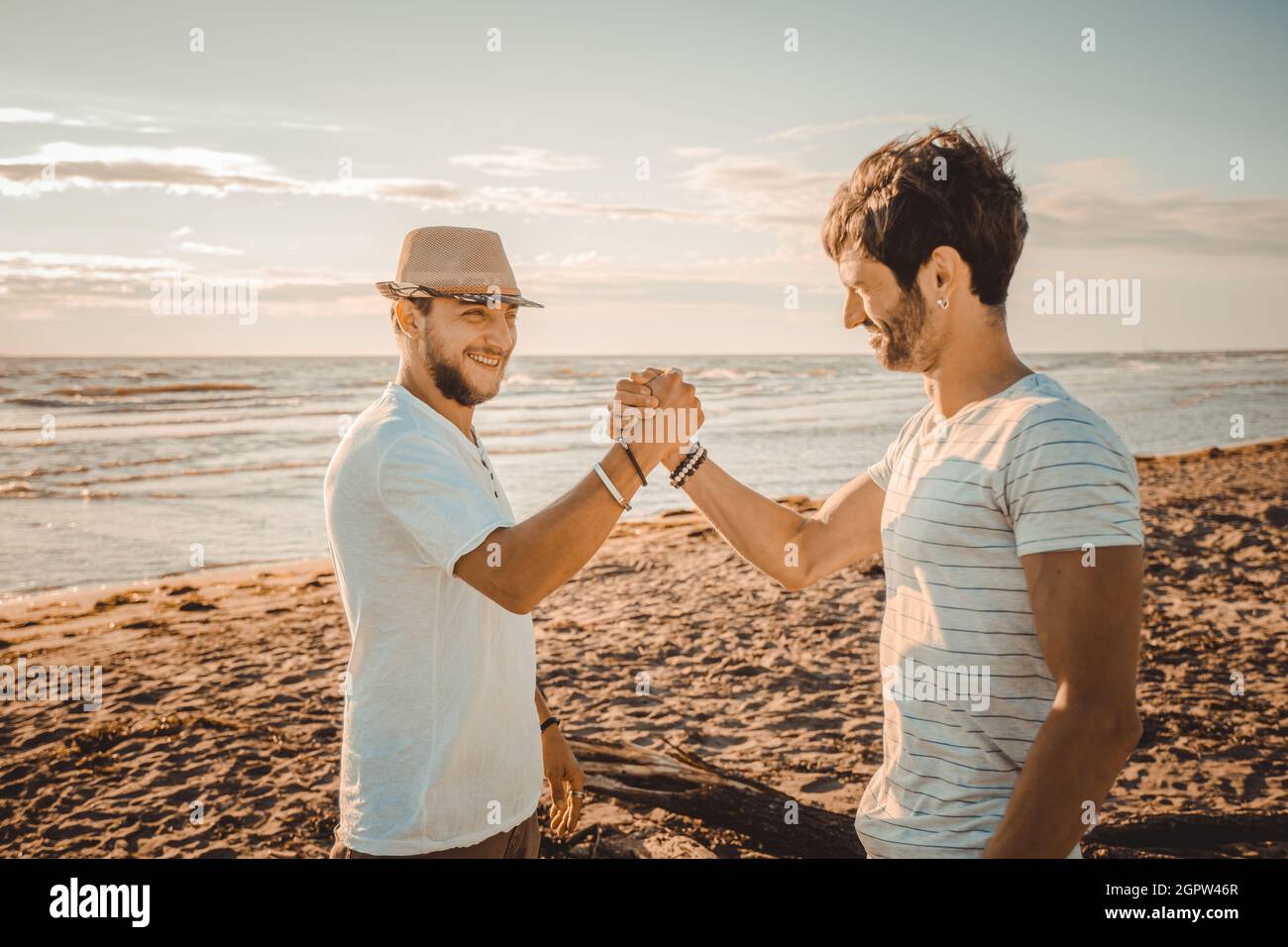 Portrait of two smiling guys on the beach shaking hands - Happy best friends greeting each other with a handshake Stock Photo