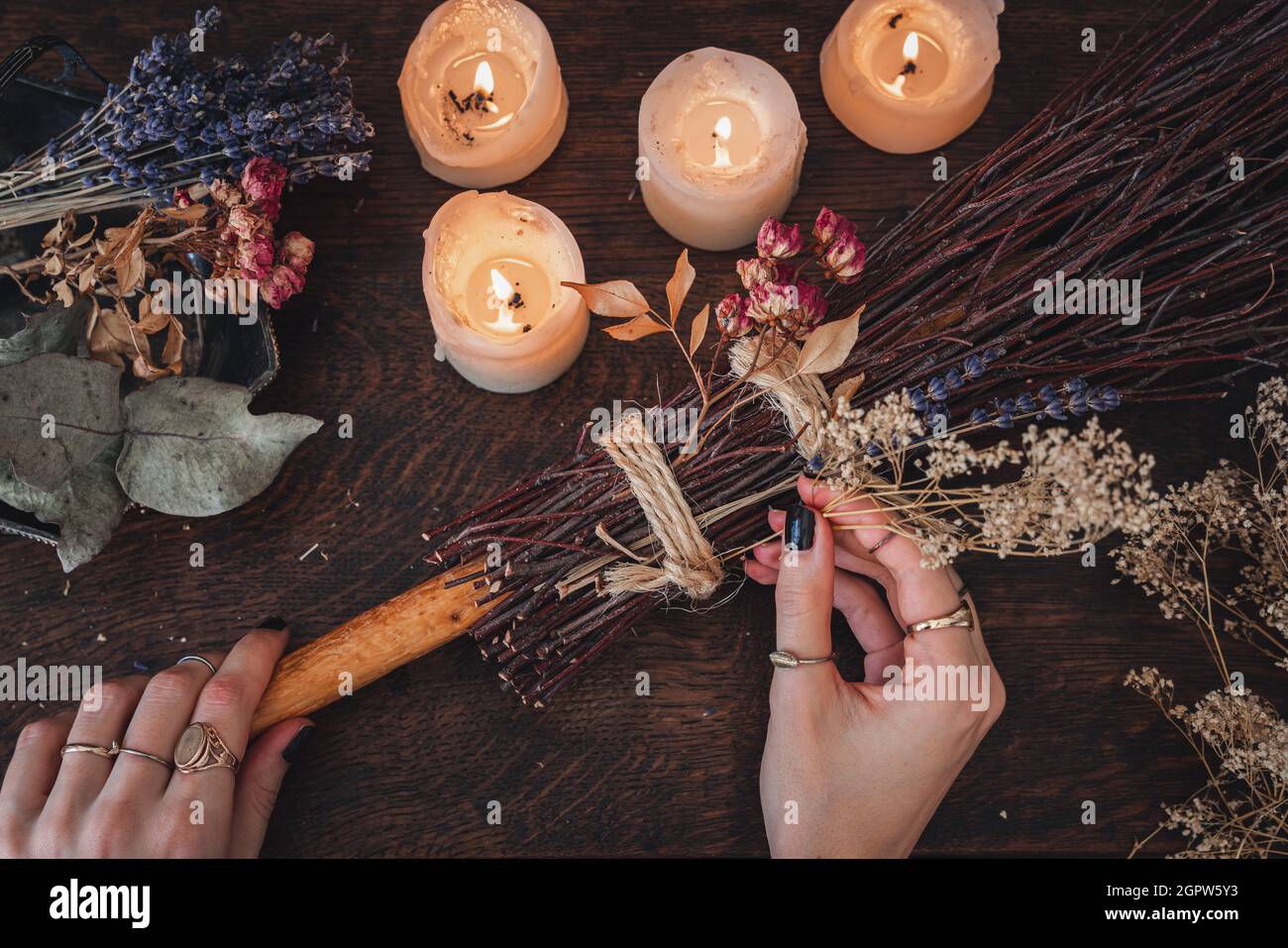 Wiccan witch decorating a DIY besom broom for Samhain celebration. Hand made broom on a dark wooden table Stock Photo
