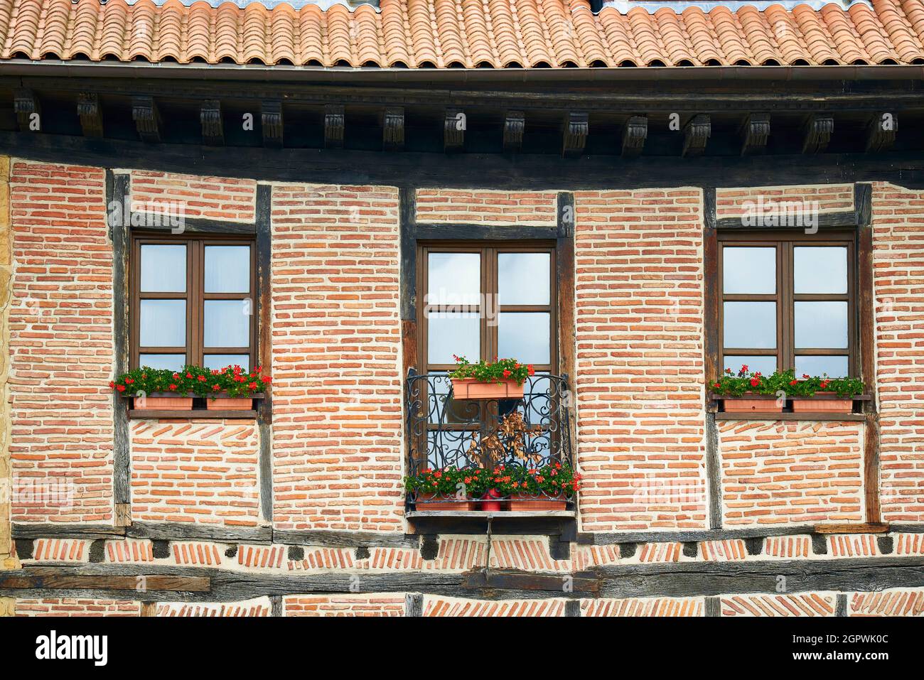 Ancient wooden building with red brick facade and flower pots in the windows and balcony Stock Photo