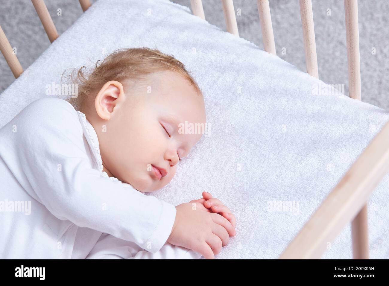 The baby sleeps safely and sweetly in his wooden crib on a terry sheet
