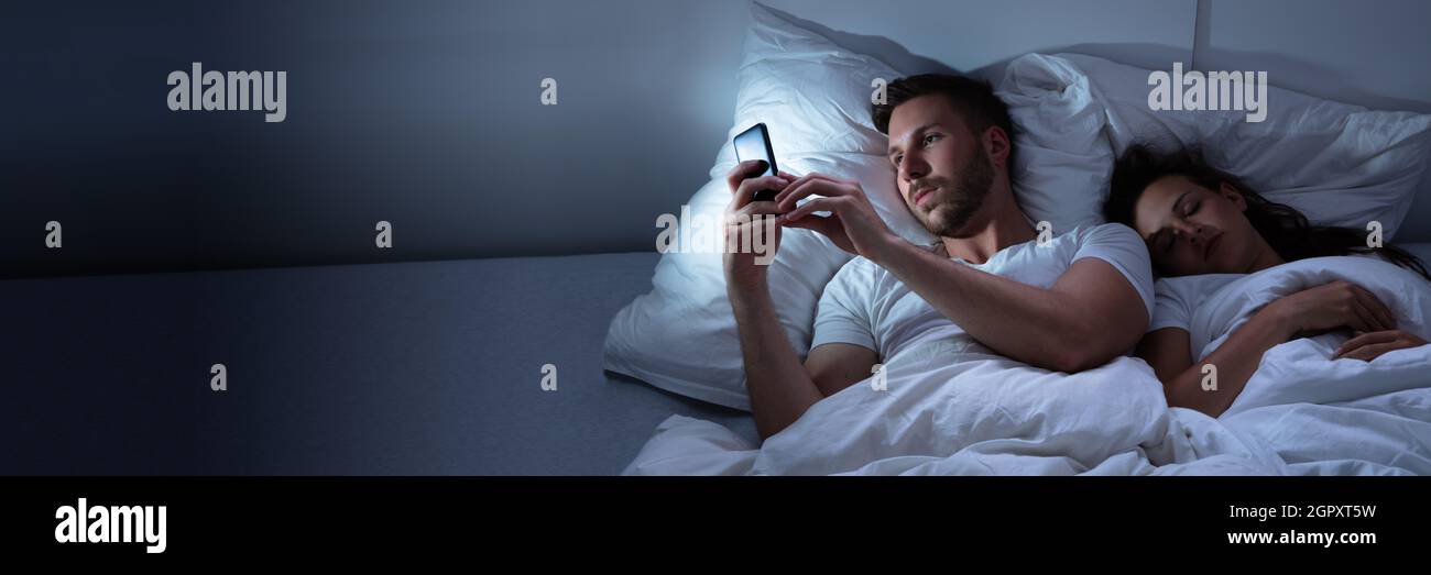 Man Cheating On Mobile Phone. Infidelity In Bed Stock Photo