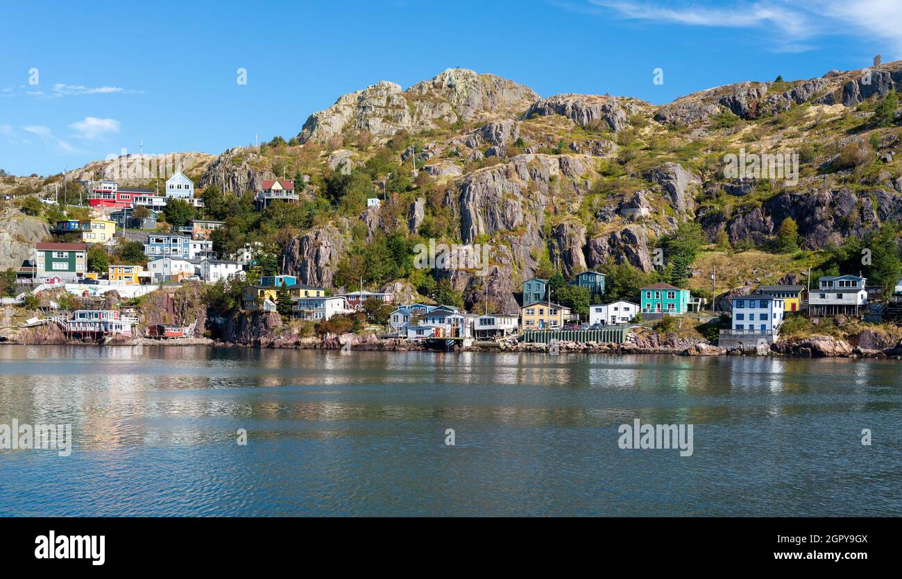 The hillside of St. John's Harbour, on a sunny day, under blue sky and white clouds. The colorful wooden houses are scattered along the hillside Stock Photo