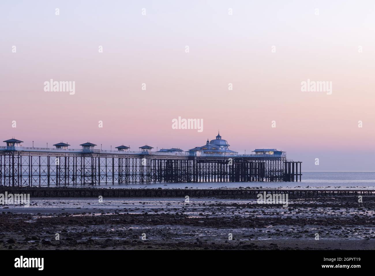 Llandudno, Conwy, UK, September 7th 2021: Just before sunrise Llandudno pier is lit by dawn light. The low tide has exposed the North Shore beach. Stock Photo