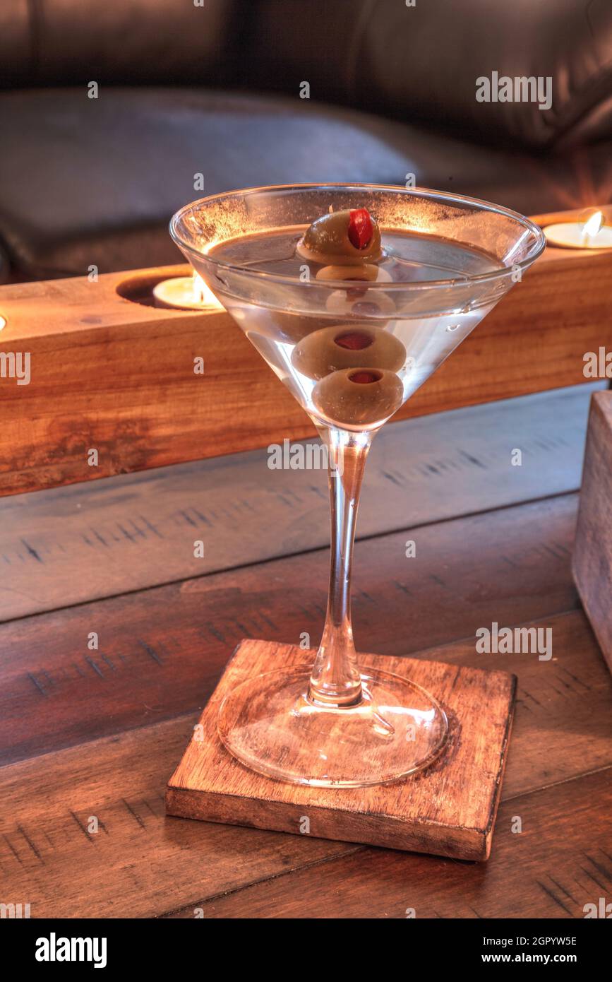 Dirty Martini With Green Pimento Olive On A Rustic Wood Coaster With Rustic Candles Behind. Stock Photo