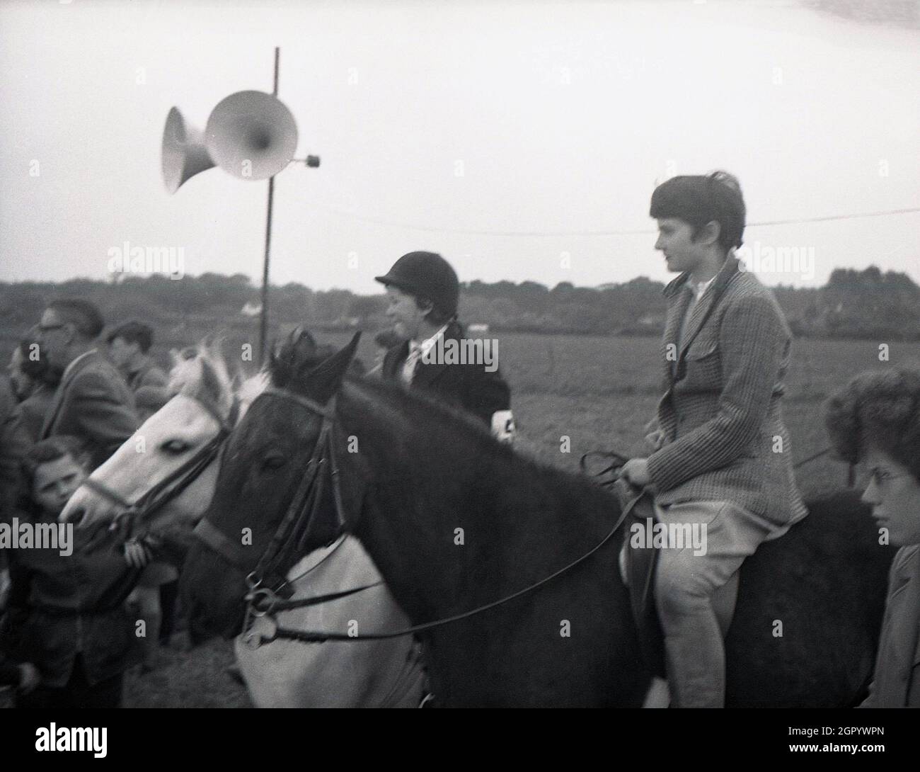 1950s, historical, two youngsters on their horses, one wearing a helmet, the other not, standing beside spectators watching an equestrian competition, West Sussex, England, UK. Stock Photo