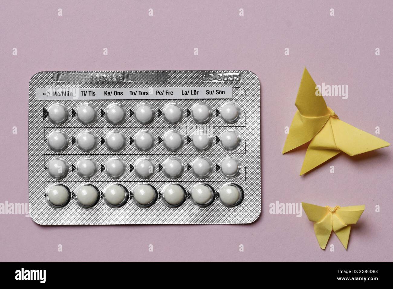 Overhead of a full chart of birth control pills and yellow origami paper butterflies on pink background Stock Photo