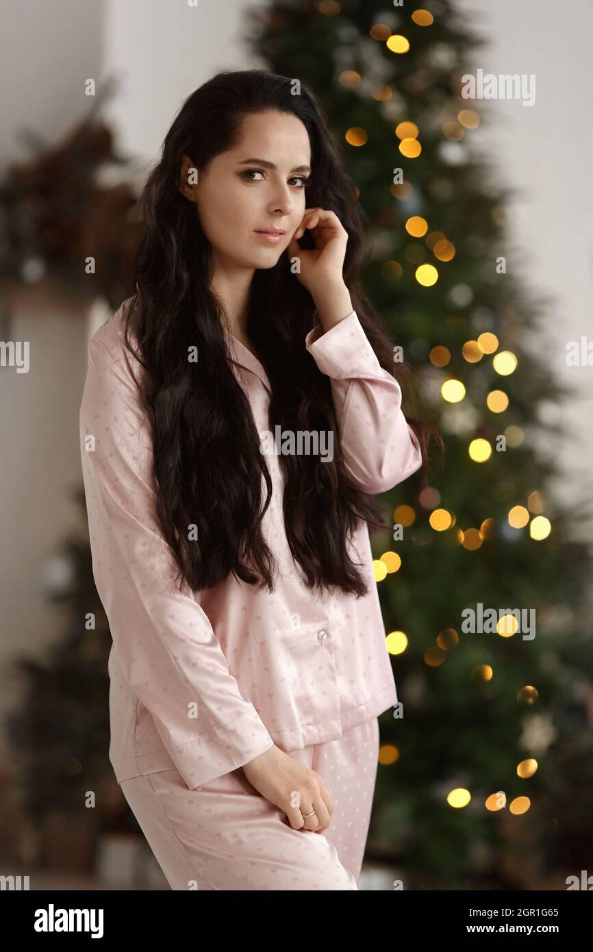 Pretty young woman with dark hair wearing modish sleepwear posing near decorated Christmas tree Stock Photo