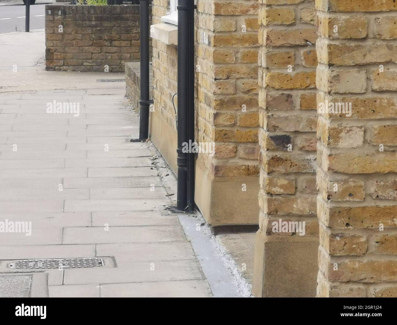 Brick built pillars and black drain pipes beside pavement in street Stock Photo