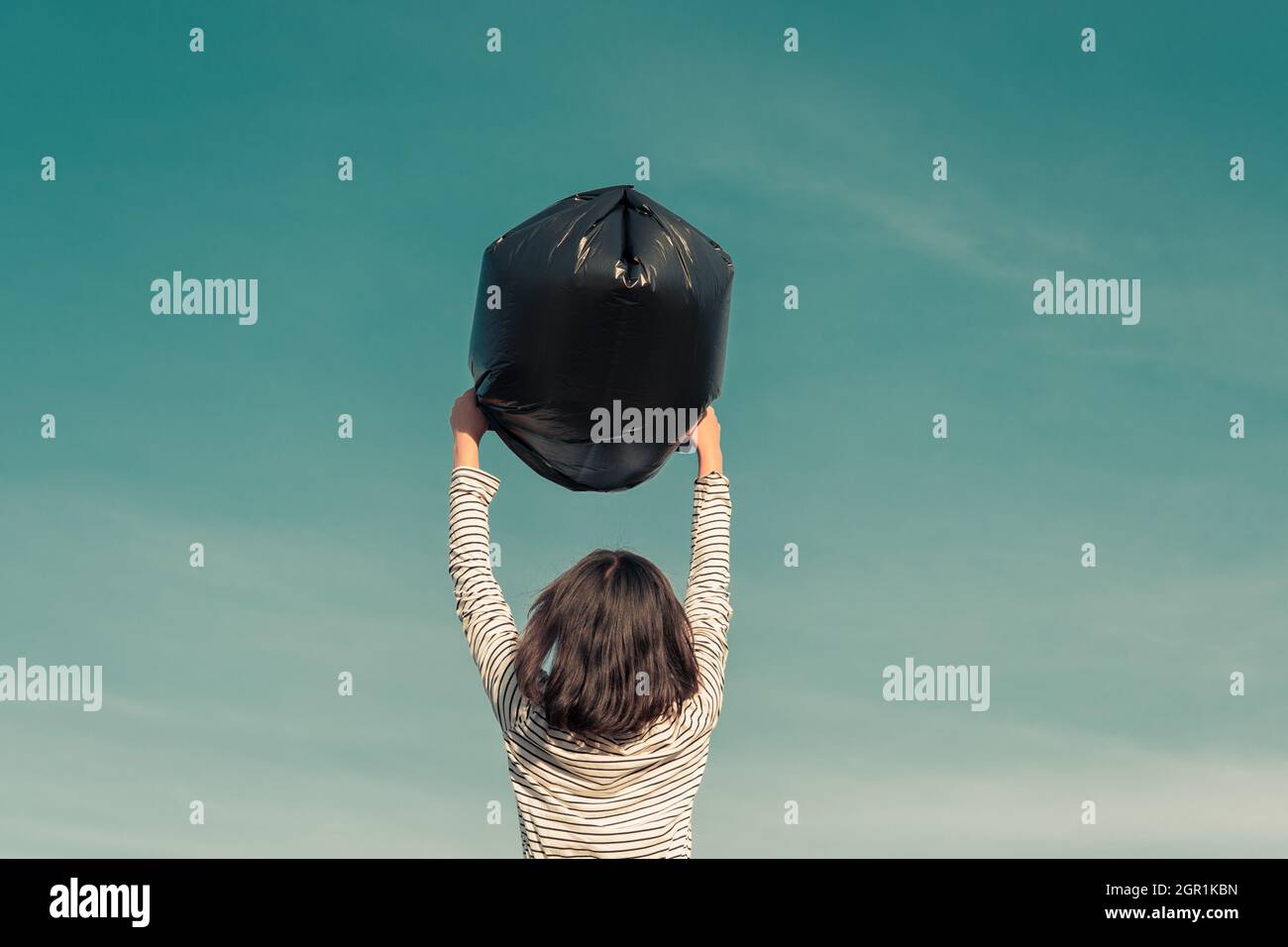 Rear View Of Girl Holding Garbage Bag Against Sky Stock Photo